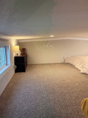 Un dormitorio con piso alfombrado, una cama, un aparador, una lámpara y un letrero en la pared que dice 'relax'.