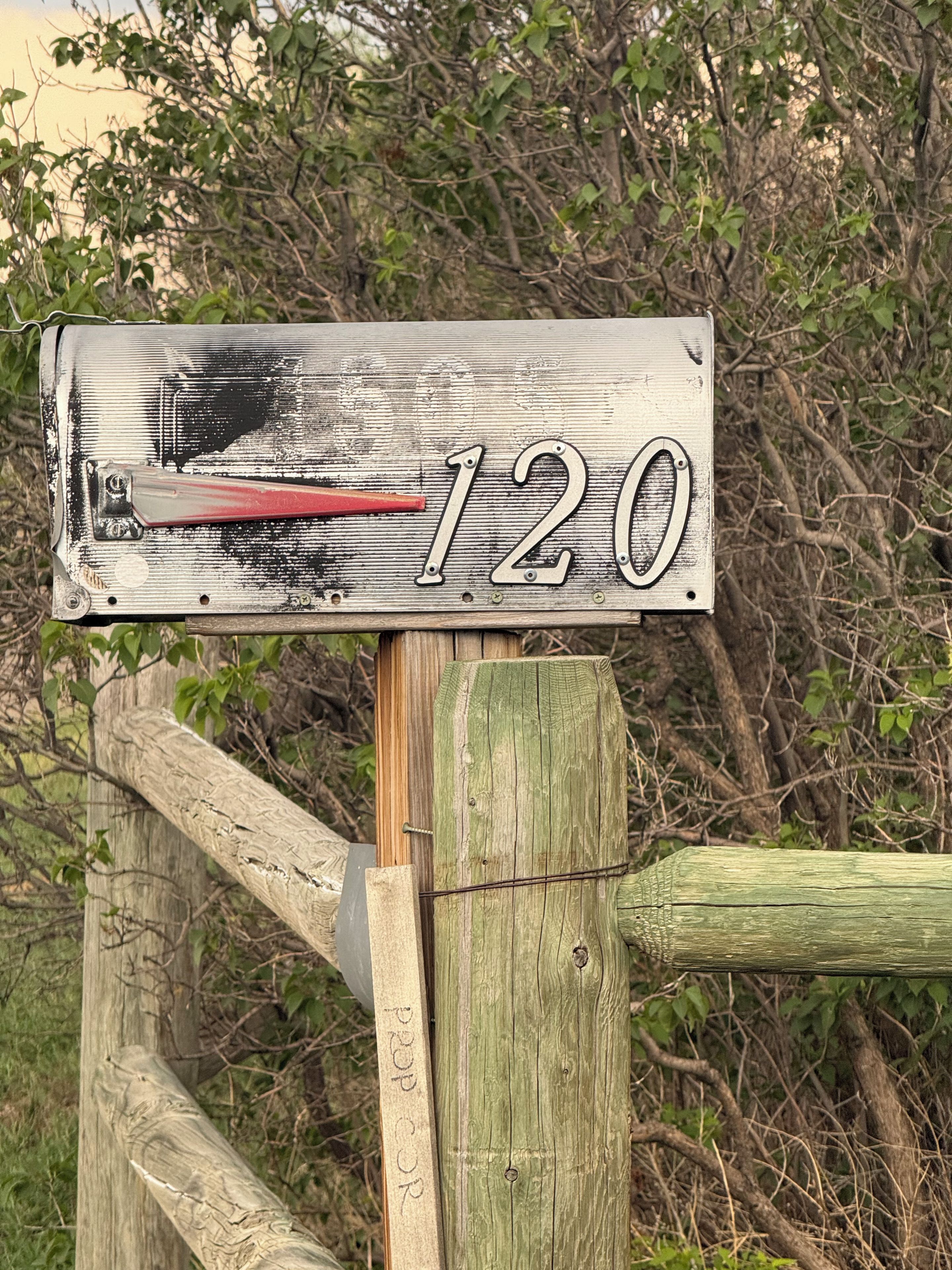 A weathered house number sign with the number 120, mounted on a wooden post with a metal bracket.