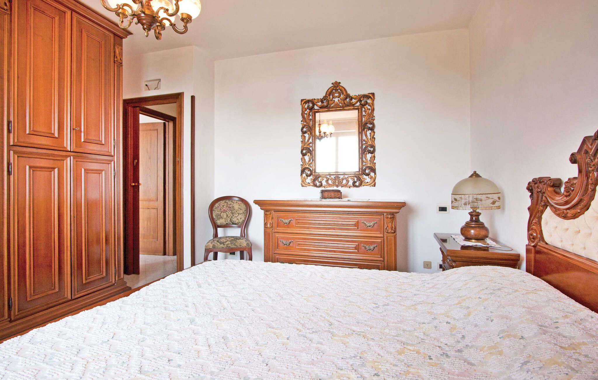 Un dormitorio con una cama grande, un aparador de madera, una silla, un espejo y una lámpara.