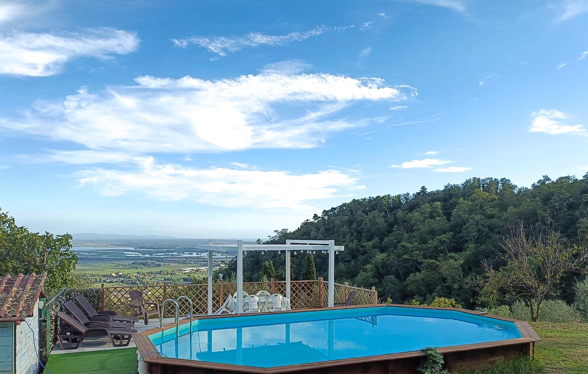 Una piscina con cubierta de madera y sillas de descanso, rodeada por una valla de madera y vistas a una ladera boscosa.