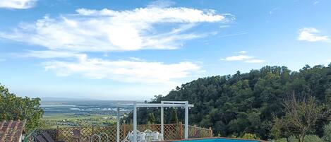 Una piscina con cubierta de madera y sillas de descanso, rodeada por una valla de madera y vistas a una ladera boscosa.