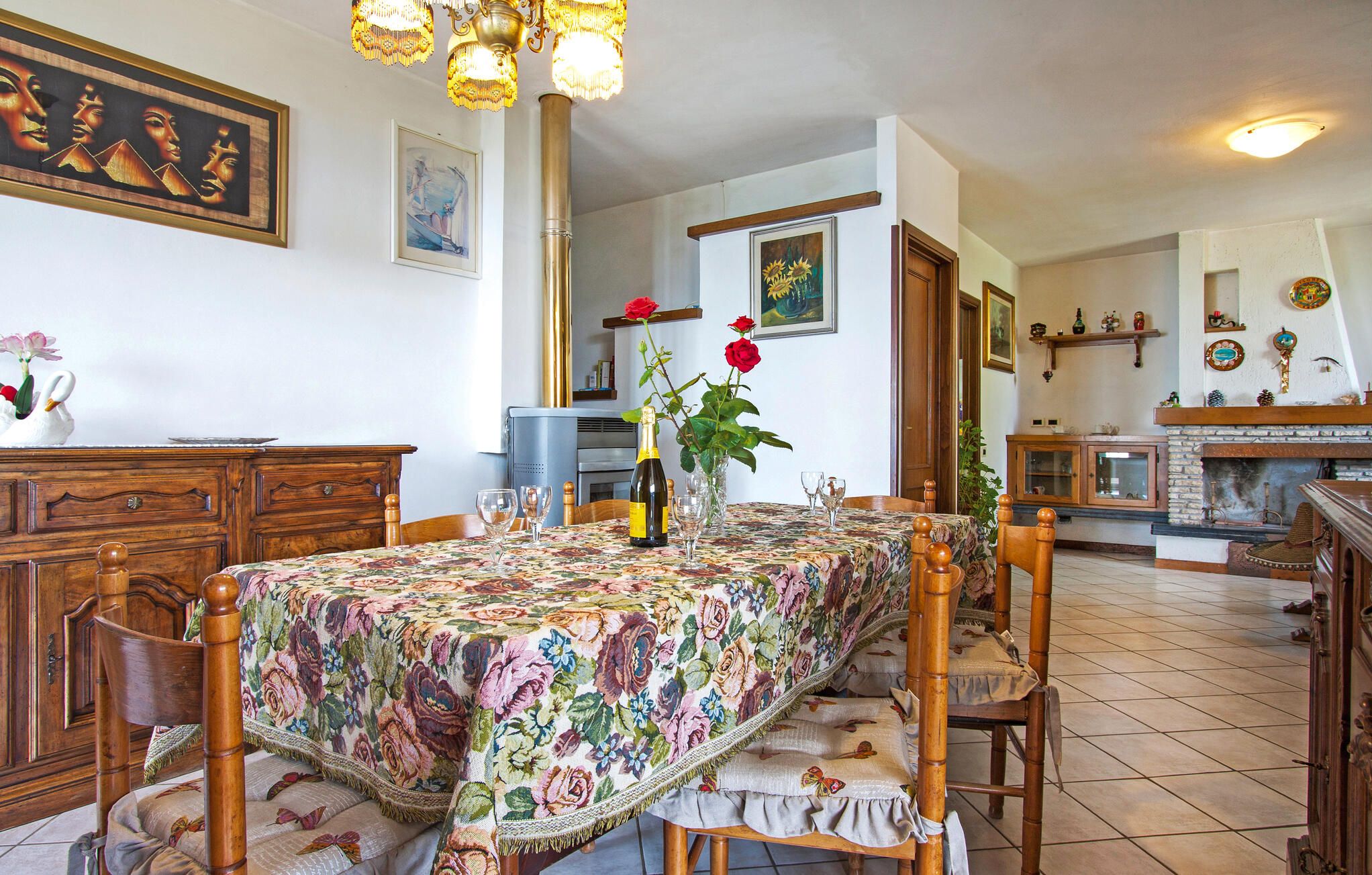 Un coin repas avec une nappe à motifs floraux, des chaises en bois, un lustre et une cheminée.
