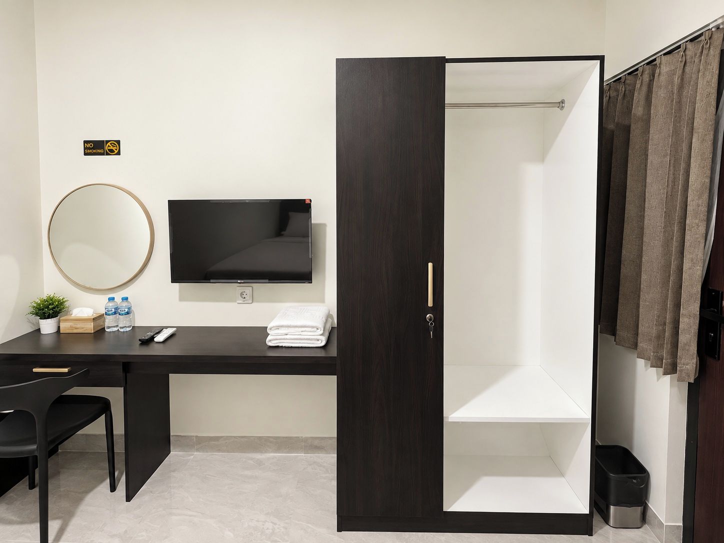 Ein Hotelzimmer mit Schreibtisch, Fernseher, Spiegel, Dusche und einem kleinen Mülleimer.