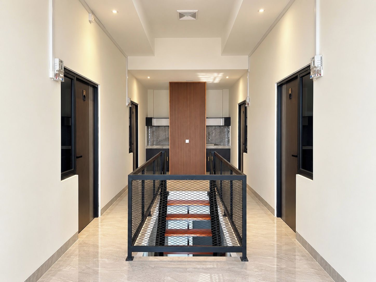 Un interior moderno con una escalera central, flanqueada por puertas y un muro de paneles de madera.