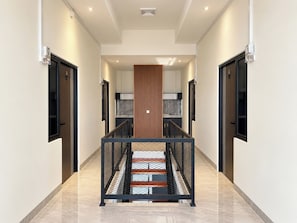Um interior moderno com uma escadaria central, ladeada por portas e um painel de madeira.