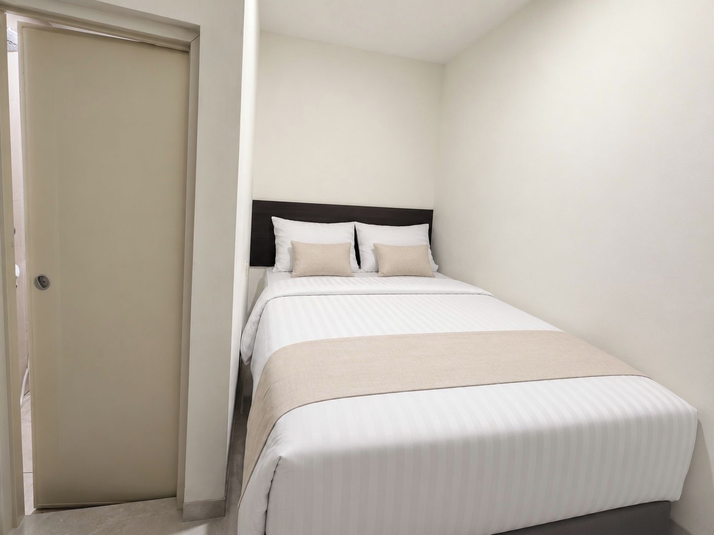 Una cama individual con cabecera, una mesita de noche y una puerta a la izquierda.
