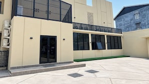 A modern building with a flat facade, large windows, and a covered outdoor area with a green lawn.