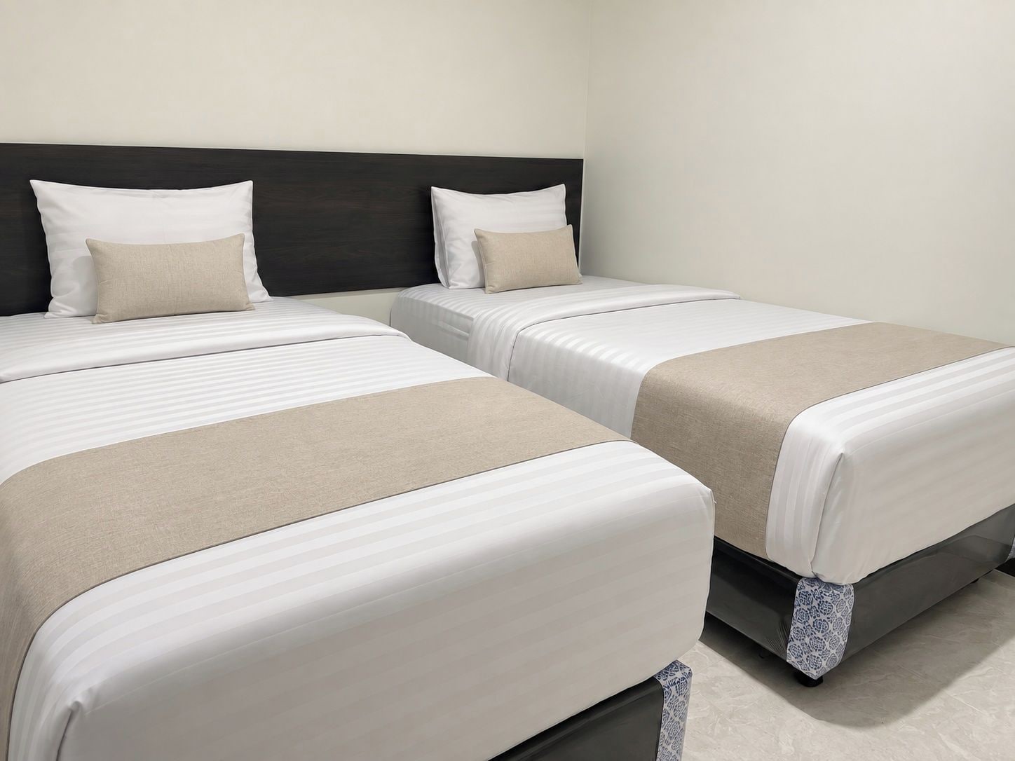 A hotel room with two beds, each with white bedding and a beige throw blanket.