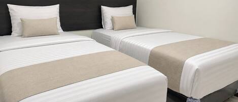 A hotel room with two beds, each with white bedding and a beige throw blanket.