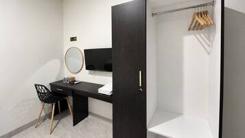 A modern hotel room with a dark wood wardrobe, a desk with a chair, a television, and a mirror.