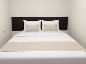 Cama com cabeceira escura, duas almofadas e colcha listrada.