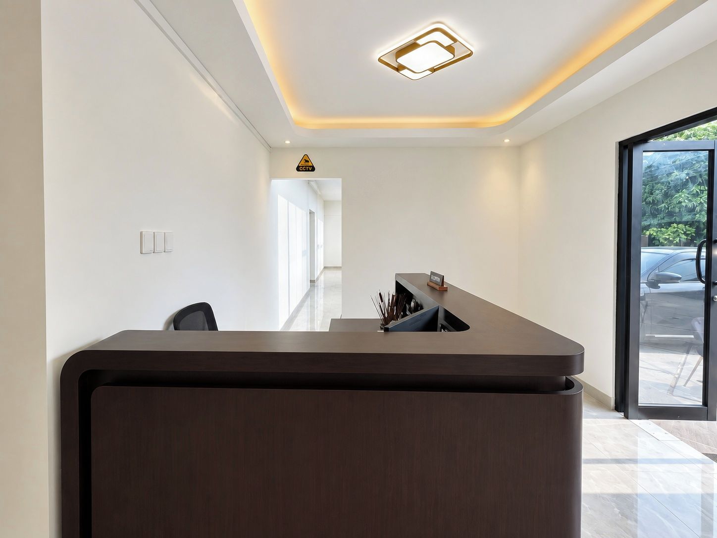 Un mostrador de recepción con diseño moderno, un lámpara en el techo y una puerta de cristal que da al exterior.