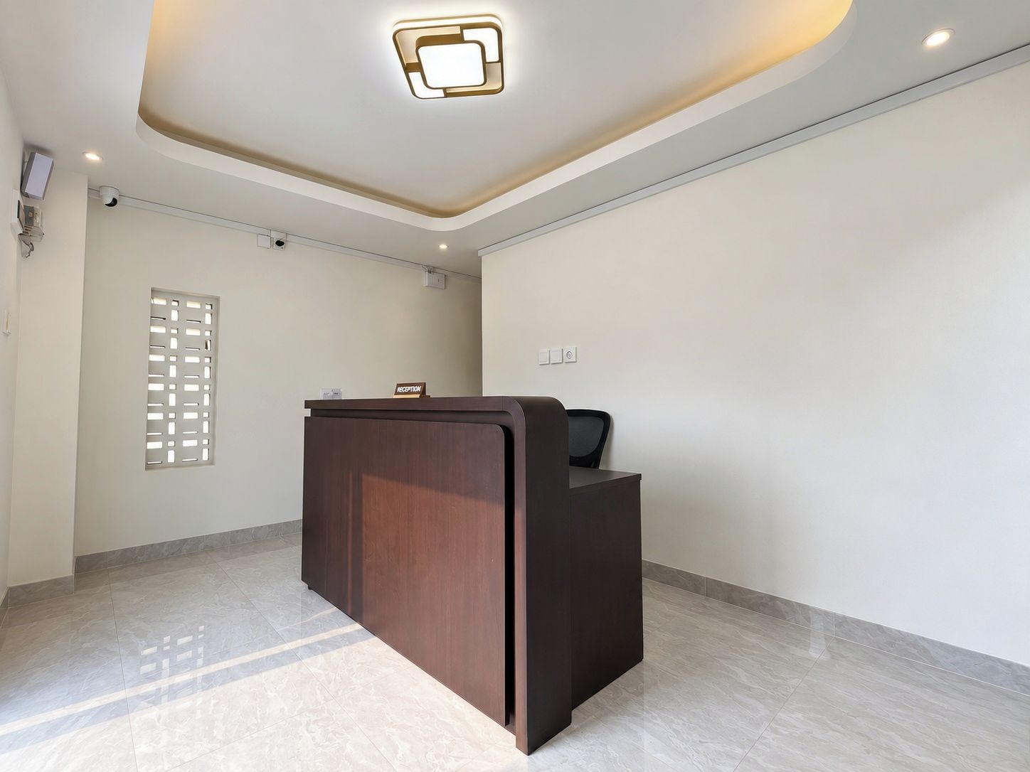 Una reception in un atrio d'hotel dal design moderno, un lampadario a soffitto e una telecamera di sicurezza a parete.