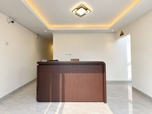 Un mostrador de recepción en el vestíbulo de un hotel con diseño moderno, un cartel que indica zona de recepción y un accesorio de iluminación en el techo.