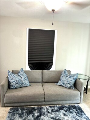 A living room with a grey sofa, two patterned throw pillows, a black abstract artwork on the wall, and a glass side table. - Pro Cleaned Home for Working Professionals (Kenosha)