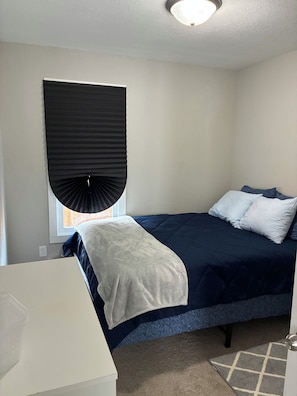 A bedroom with a bed, a window with blinds, a bedside table, and a rug. - Pro Cleaned Home for Working Professionals (Kenosha)
