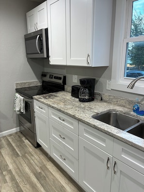 A kitchen with white cabinets, a stainless steel sink, a microwave, a stove, and a coffee maker. - Pro Cleaned Home for Working Professionals (Kenosha)