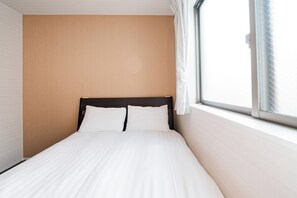 A single bed with white bedding in a room with wooden panel walls and a window with white curtains. - Luce Kamiikebukuro (toshima-city)