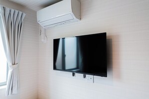 A flat-screen TV mounted on a wall with a power outlet below it. - Luce Kamiikebukuro (toshima-city)