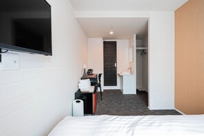 A hotel room with a bed, a desk with a chair, a television, a bathroom with a sink and mirror, and a hallway leading to another room. - Luce Kamiikebukuro (toshima-city)