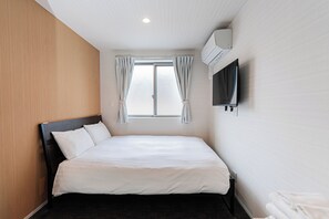 A hotel room with a bed, a flat-screen TV mounted on the wall, a window with curtains, and an air conditioning unit. - Luce Kamiikebukuro (toshima-city)