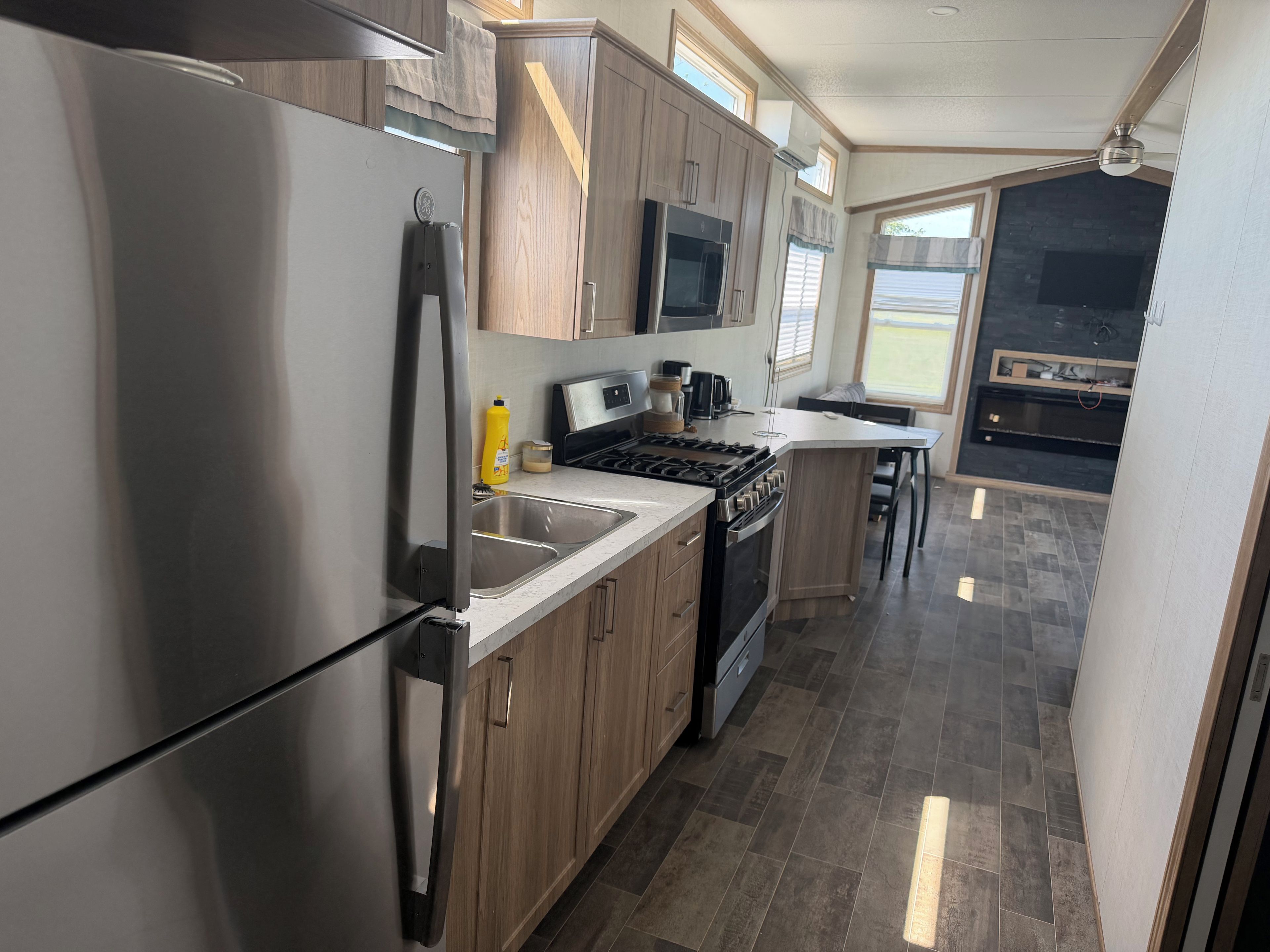 A modern kitchen with stainless steel appliances, wooden cabinets, and a large window providing natural light.