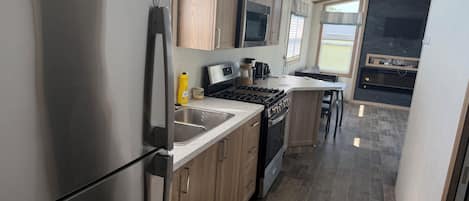 A modern kitchen with stainless steel appliances, wooden cabinets, and a large window providing natural light.