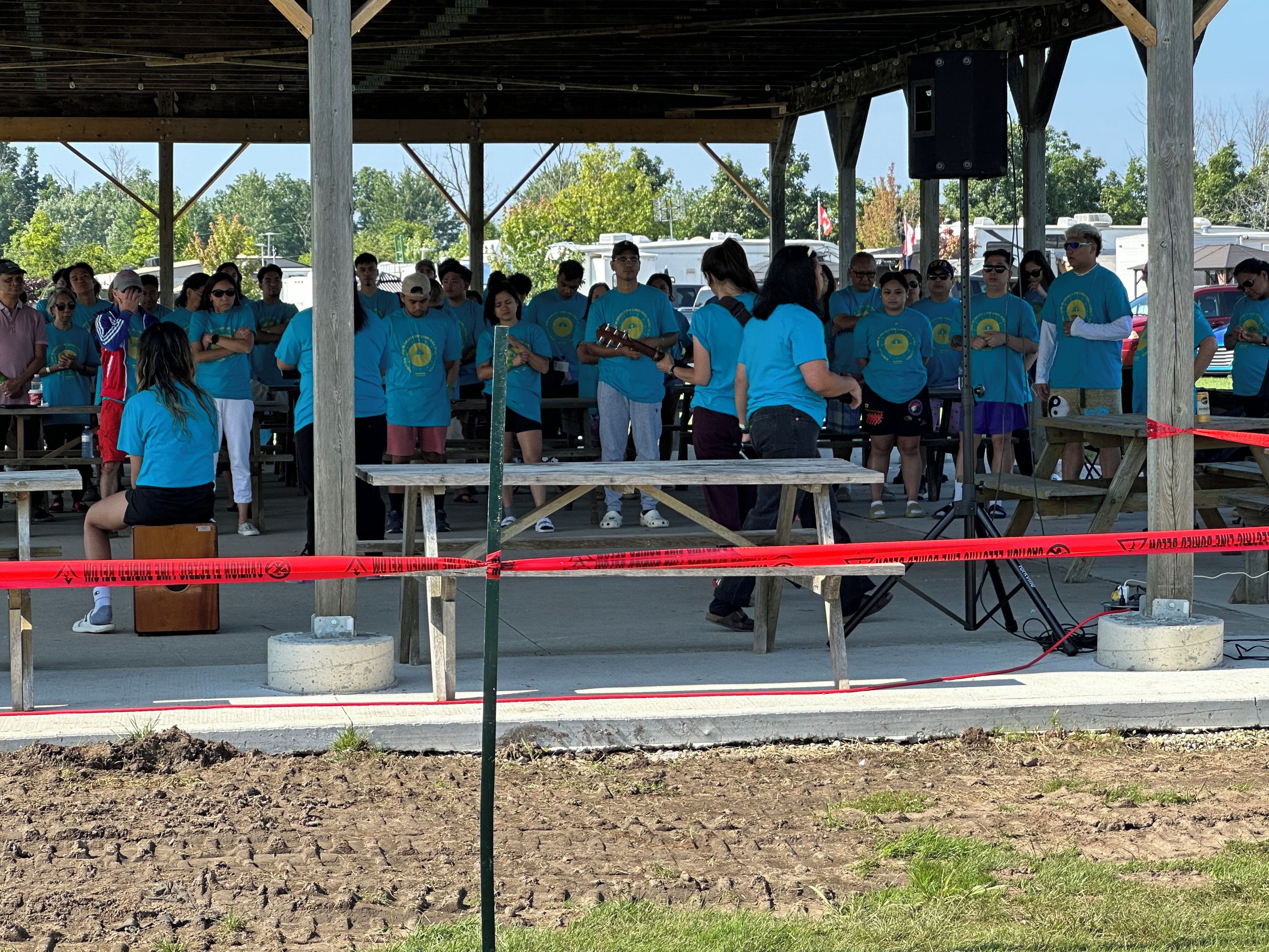Un groupe de personnes portant des chemises bleues s’est rassemblé sous une structure en bois, où se trouvaient des tables et des bancs.