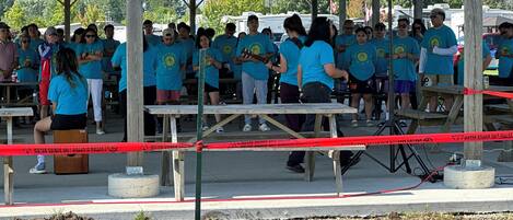 Un groupe de personnes portant des chemises bleues s’est rassemblé sous une structure en bois, où se trouvaient des tables et des bancs.