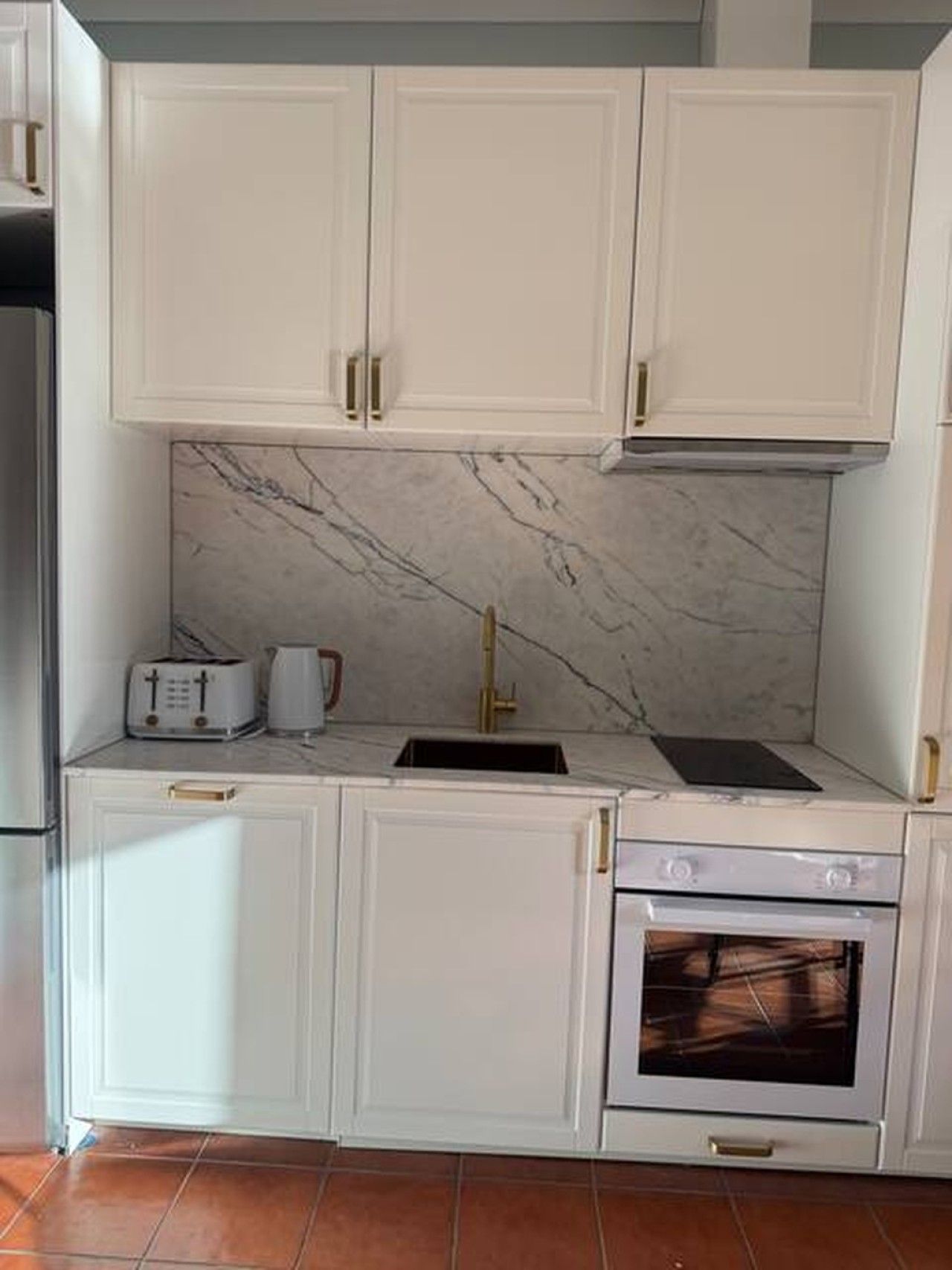 A kitchen with white cabinetry, a marble backsplash, a built-in oven, and a toaster.