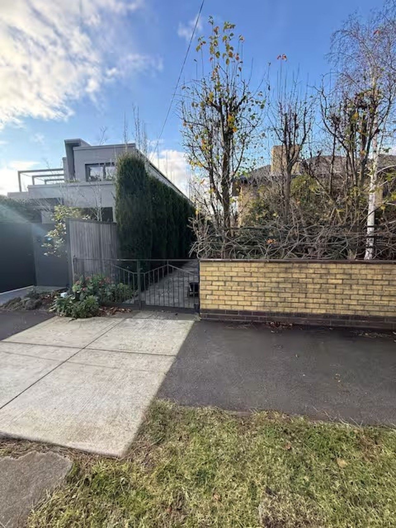 Una propiedad residencial con camino de entrada pavimentado, pared de ladrillo y portón metálico.