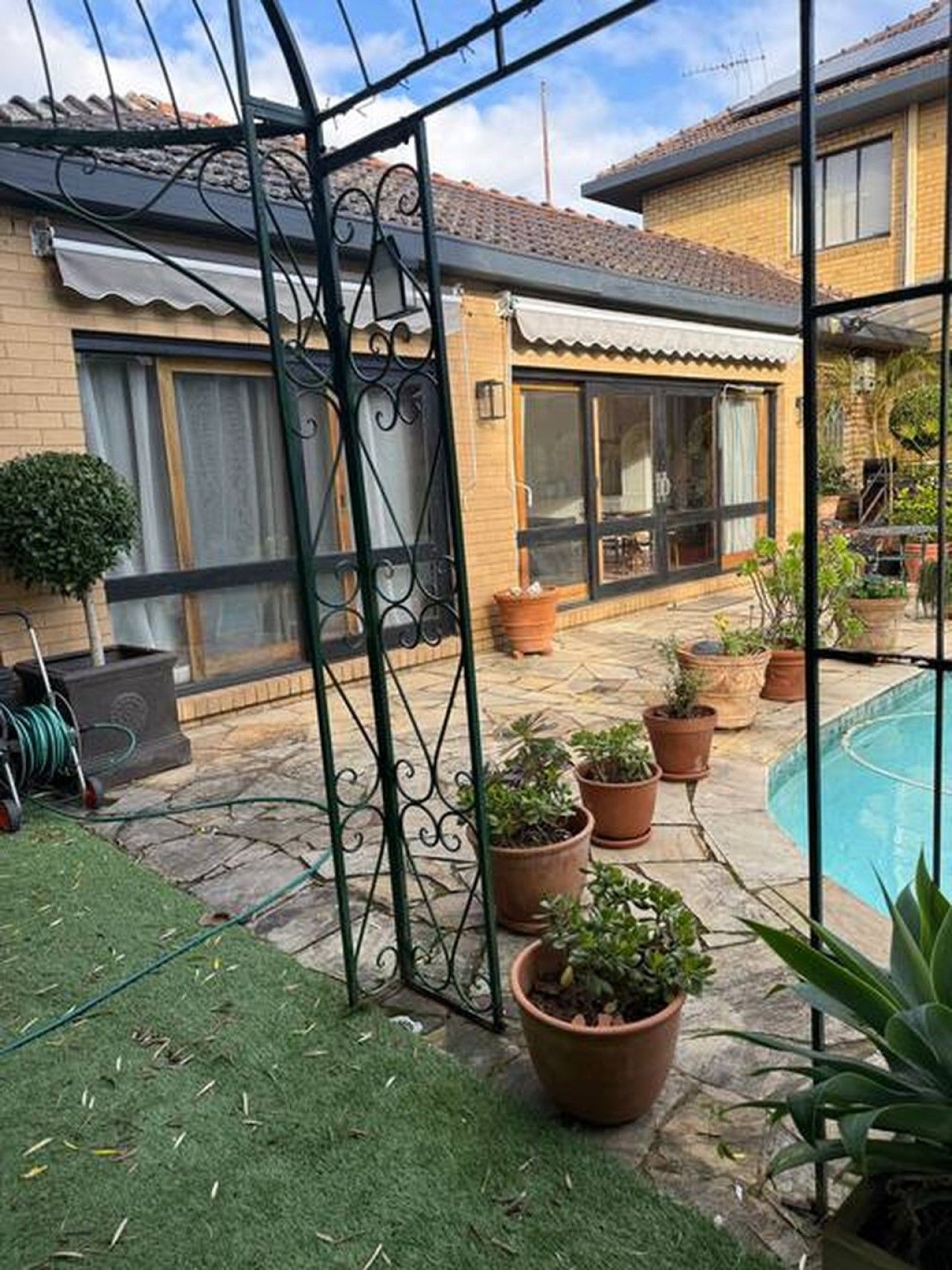 A courtyard with a swimming pool, potted plants, and a metal gate.