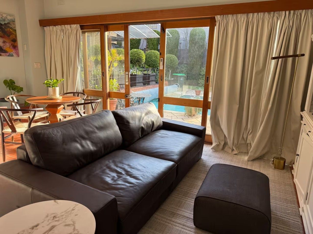 A modern living room with a leather sofa, a round coffee table, and a view of a garden through large windows.
