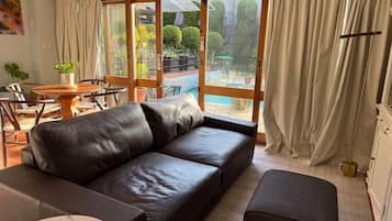 A modern living room with a leather sofa, a round coffee table, and a view of a garden through large windows.