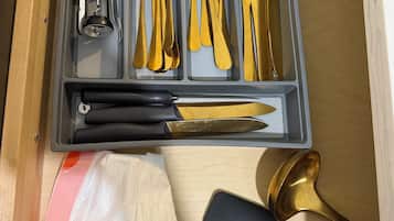 A drawer containing a set of gold-colored cutlery including spoons, forks, and knives, along with a bottle opener and a black-handled knife.