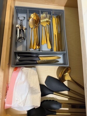 A drawer containing a set of gold-colored cutlery including spoons, forks, and knives, along with a bottle opener and a black-handled knife. - Bright apartment in Tavernier with Ac and kitchen, Tavernier key largo (Tavernier)