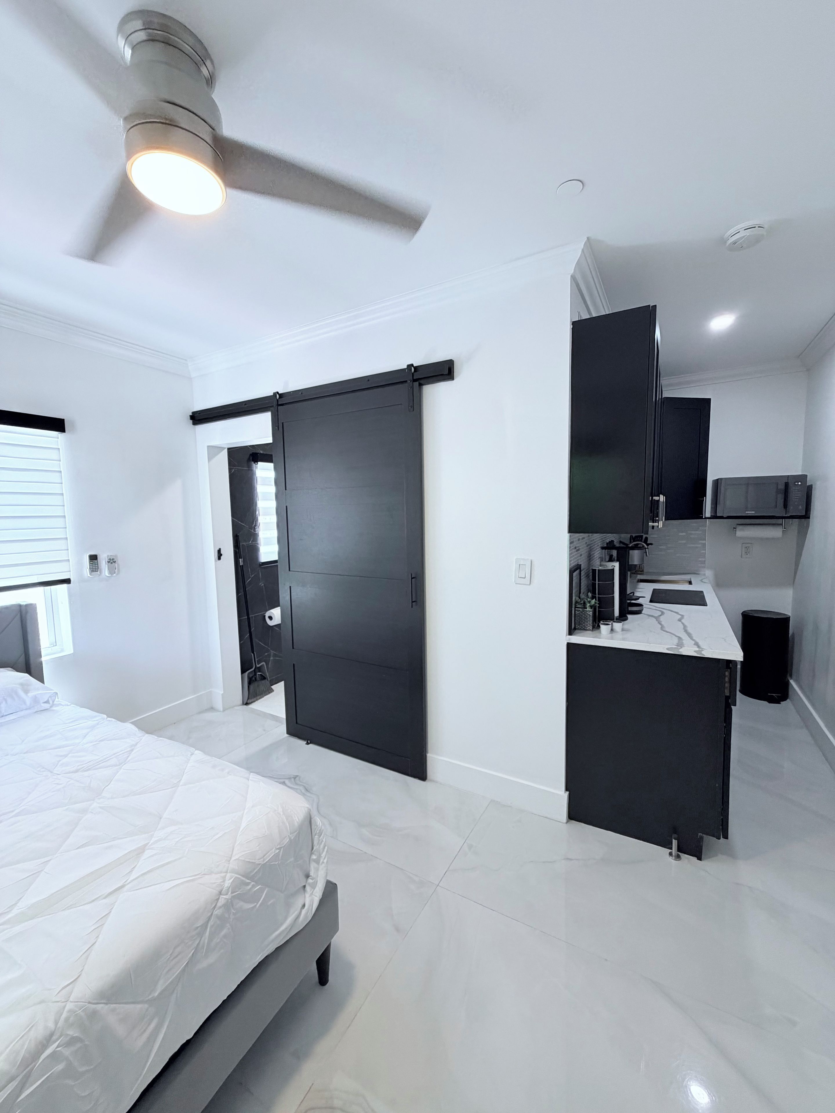 A modern bedroom with a bed, a ceiling fan, and a sliding door leading to a kitchen area.