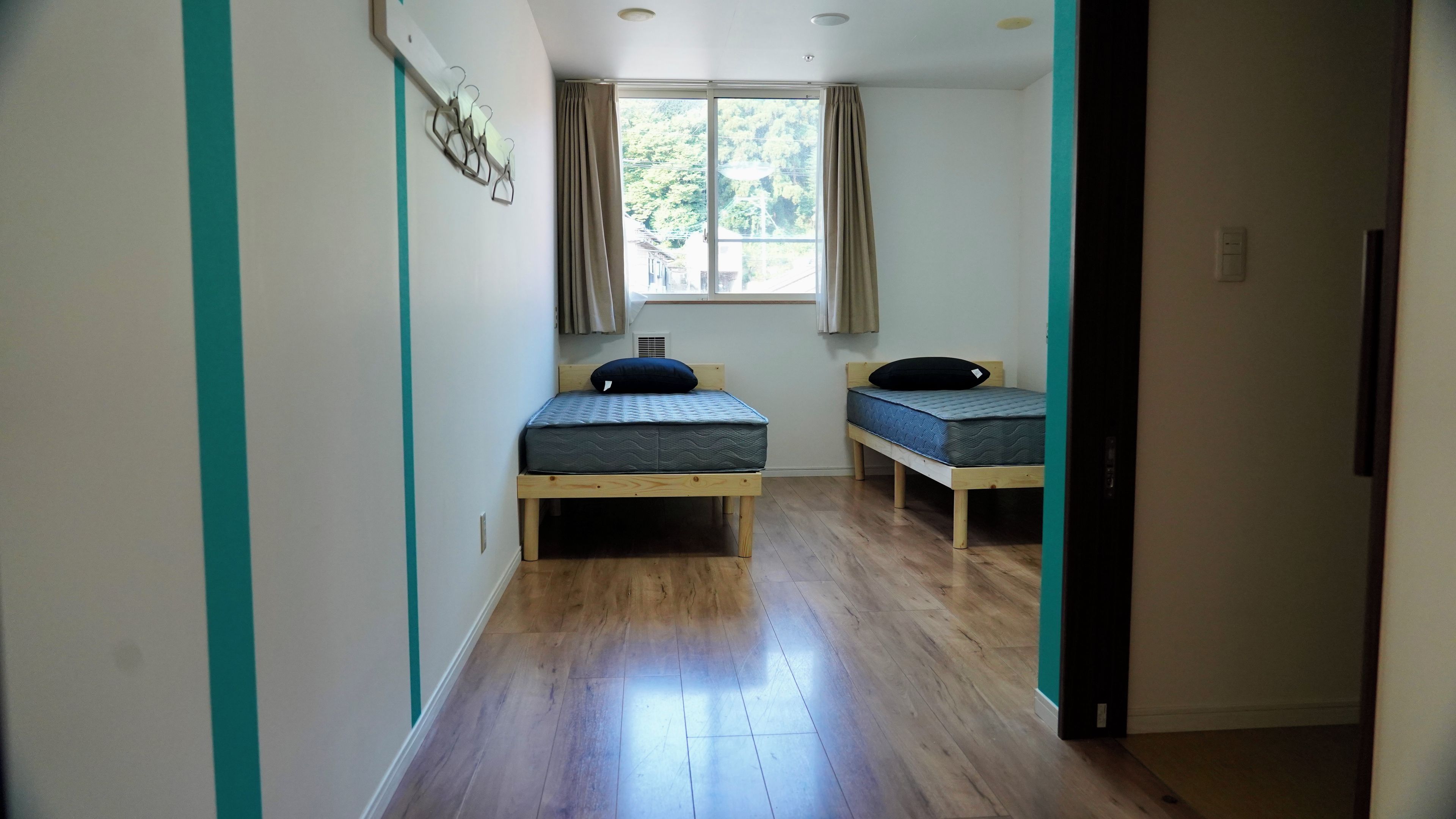 A room with two single beds, a window with curtains, and a wooden floor.