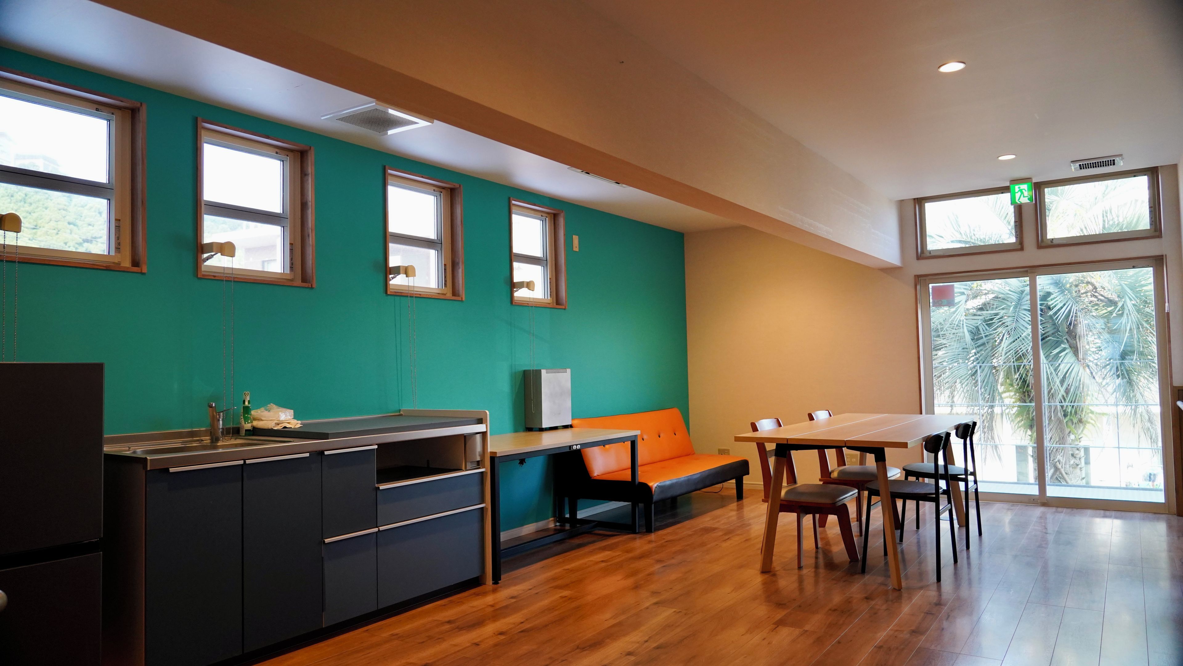 A modern kitchen with a dining area, wooden flooring, and large windows.
