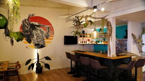 A modern bar area with a wooden counter, bar stools, and a variety of plants.
