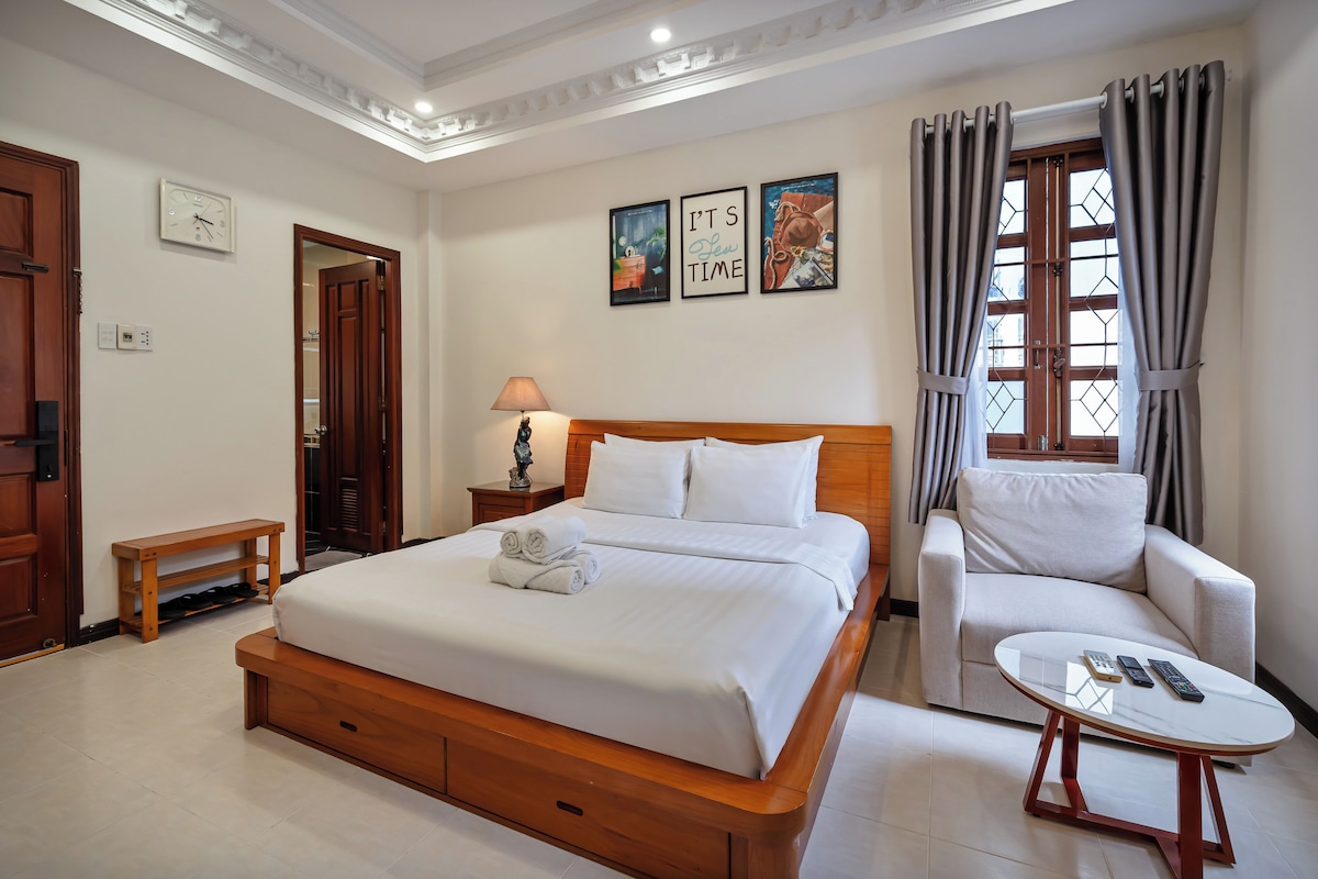 Ein Hotelzimmer mit Bett, Stuhl, kleinem Tisch und einem Fenster mit Vorhängen.
