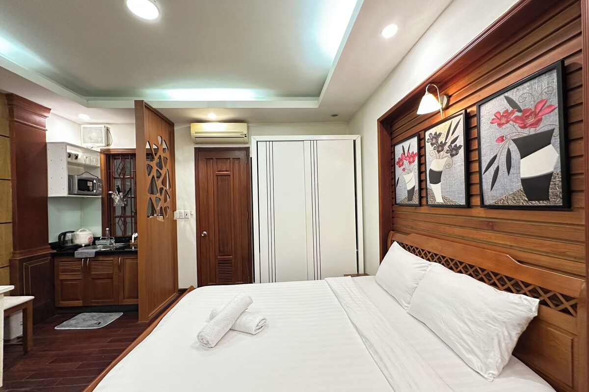 Ein Hotelzimmer mit Bett, Holz-Kopfteil, Kleiderschrank, Küchenzeile und Bildern an der Wand.
