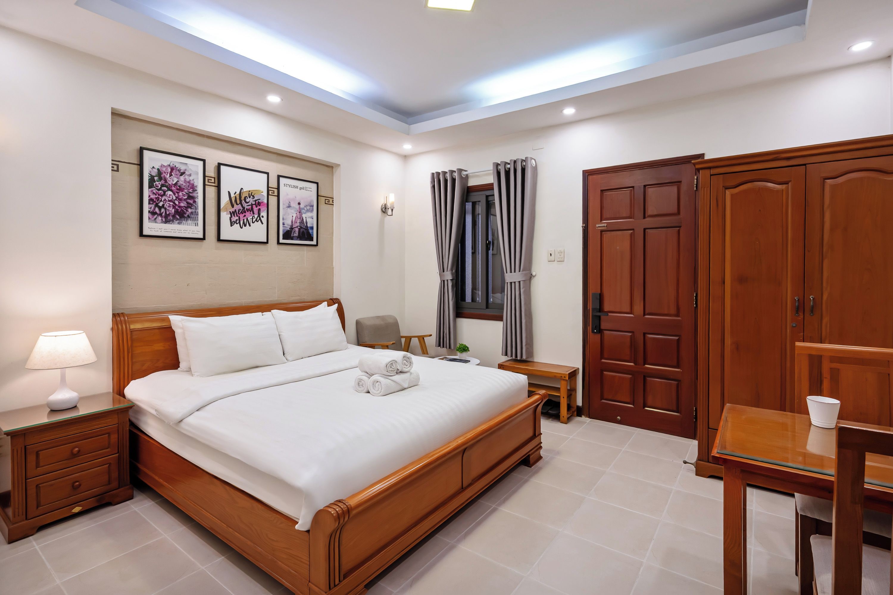 Una habitación de hotel con una cama de madera, una mesita de noche con lámpara, un escritorio con silla y un armario.
