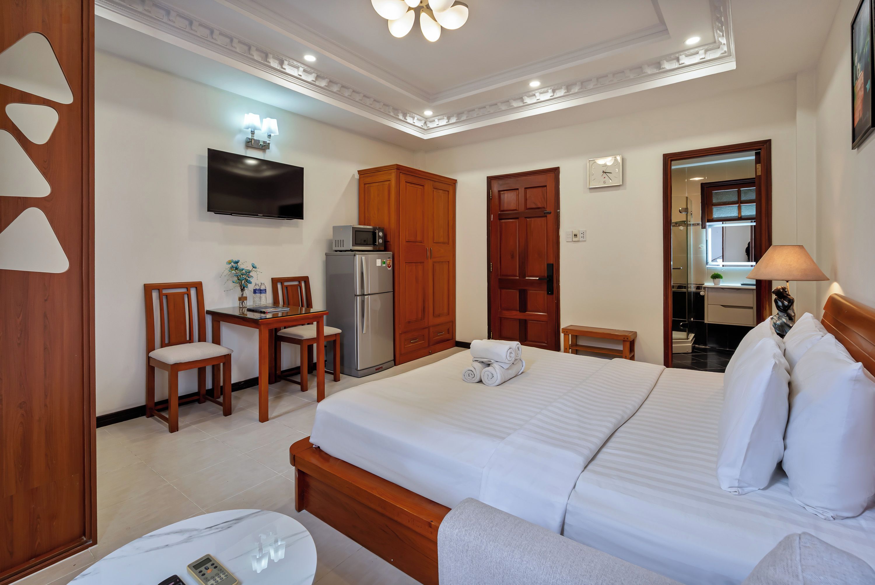 A hotel room with a bed, a desk with a chair, a refrigerator, a microwave, a television, and a bathroom visible through an open door.