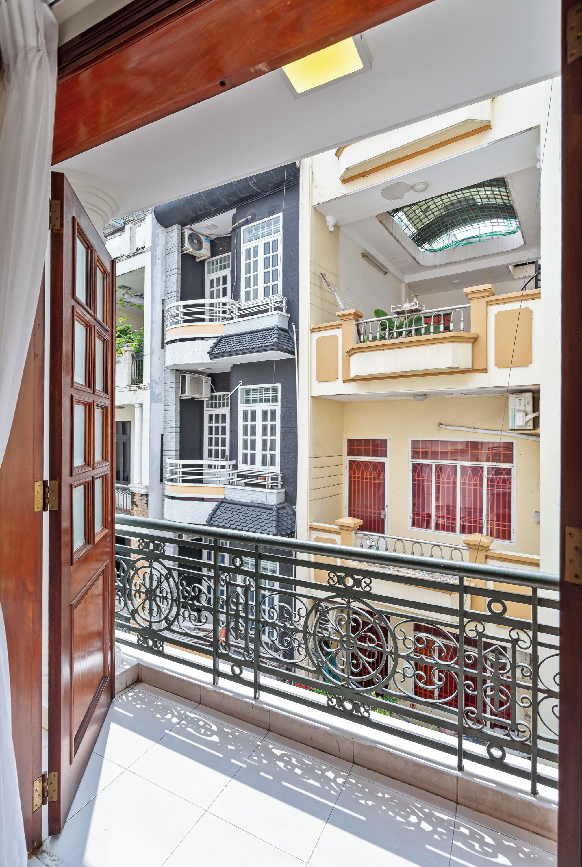 A balcony with a wrought iron railing, a wooden door, and a view of neighboring buildings with multiple windows and balconies.