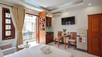 A hotel room with a bed, a dining table with chairs, a kitchen area, and a TV mounted on the wall.