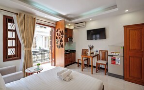 Habitación de hotel con cama, una mesa de comedor con sillas, una zona de cocina y un televisor montado en la pared.