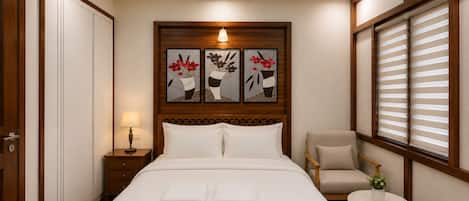 Habitación de hotel con una cama, una mesita de noche, una silla, una pequeña mesa con una planta y una obra de arte en la pared.