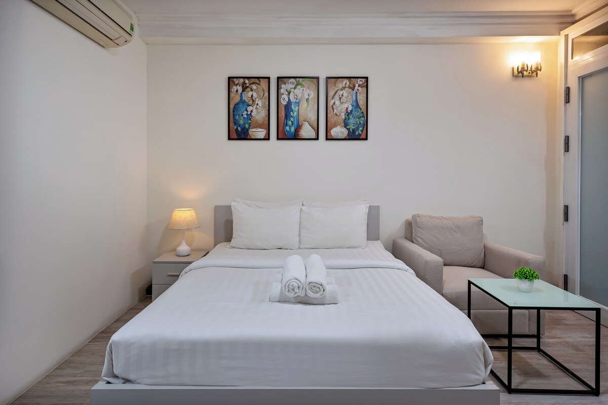 Ein Hotelzimmer mit einem Bett, einem Nachttisch, einer Lampe, einem Sessel und einem kleinen Tisch mit einer Pflanze.