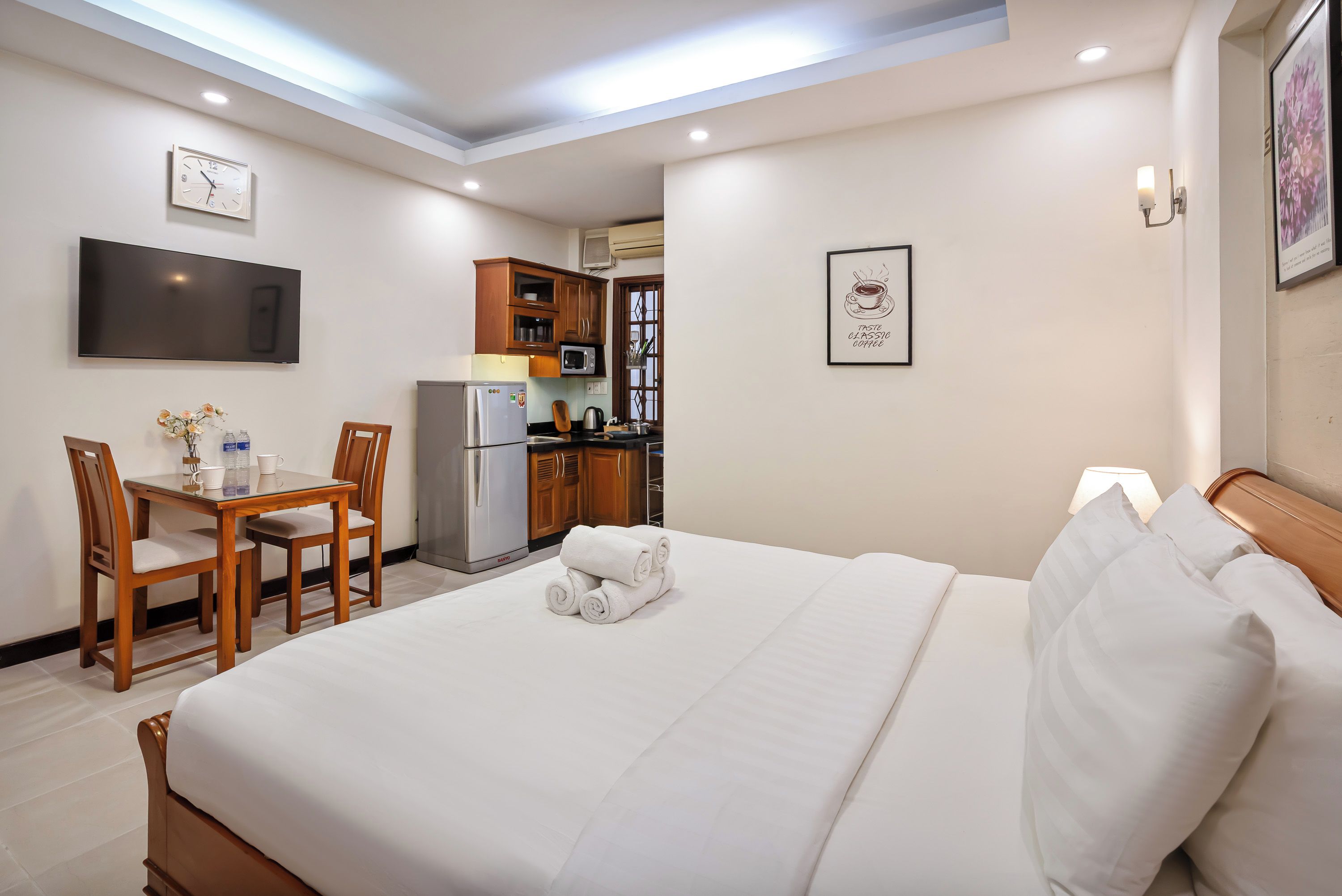 A hotel room with a bed, a desk with chairs, a refrigerator, a microwave, and a television.